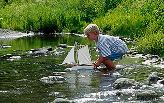 Side profile of a boy playing with a paper boat